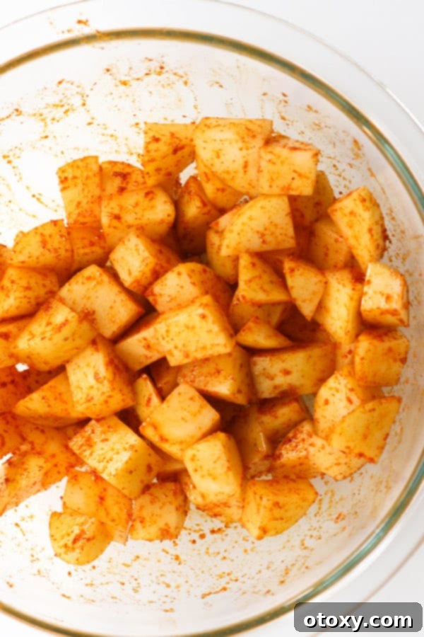 Diced potatoes seasoned with spices and olive oil in a clear glass bowl, ready for the air fryer.