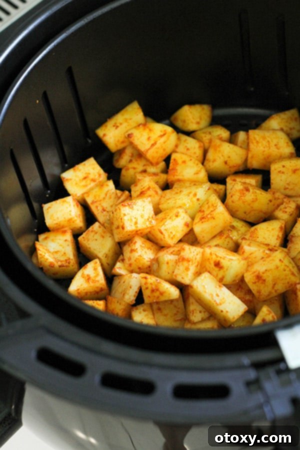 Seasoned diced potatoes cooking in an air fryer basket, achieving a golden crisp.