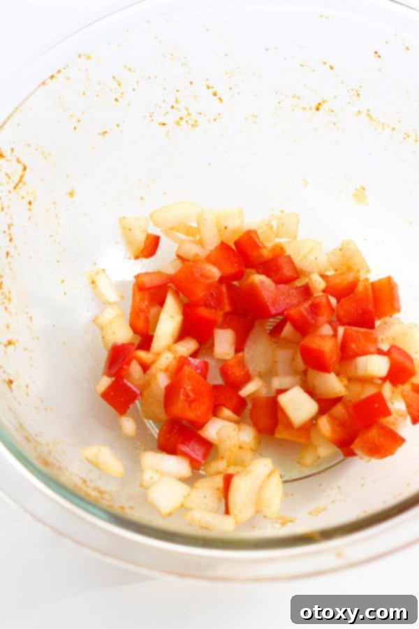 Diced onion and capsicum (bell pepper) in a glass bowl, seasoned with residual spices and oil.