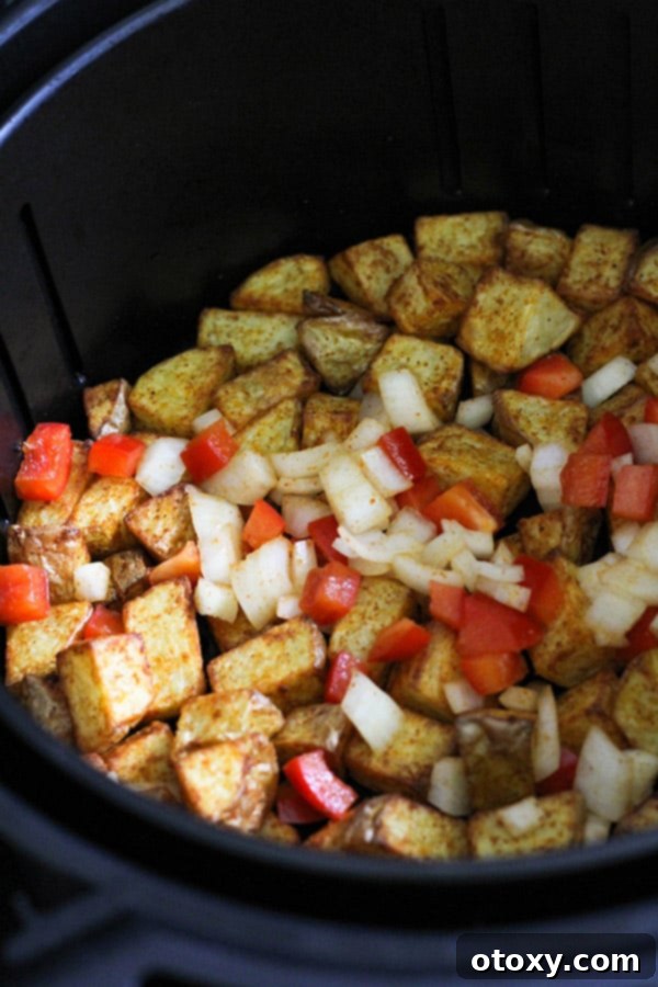 A mix of golden crispy potatoes, red capsicum, and onion cooking together in an air fryer basket.