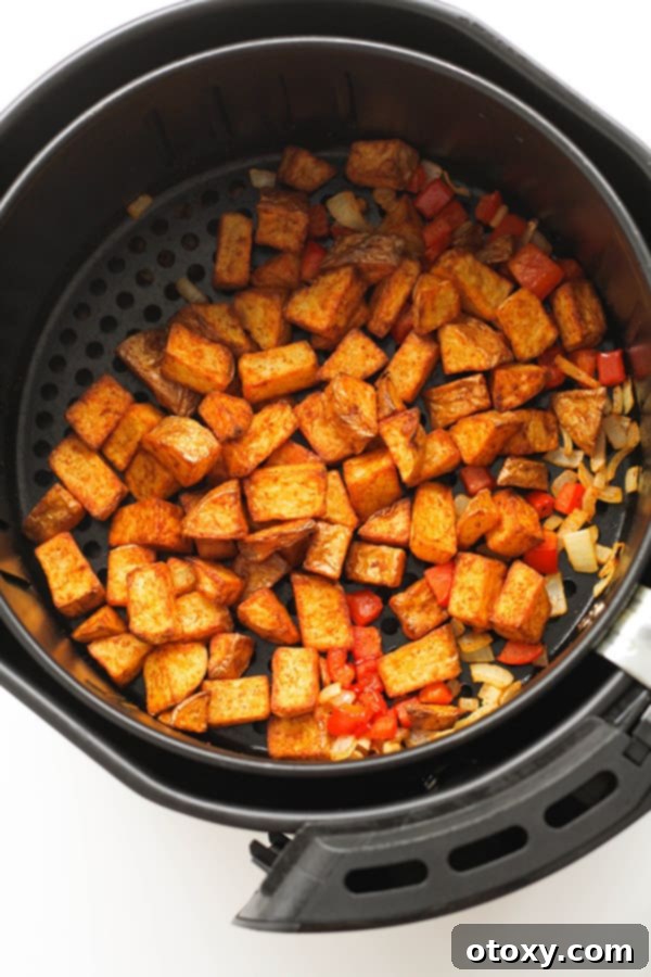 Close-up of freshly air-fried crispy breakfast potatoes with vibrant vegetables in the air fryer basket.