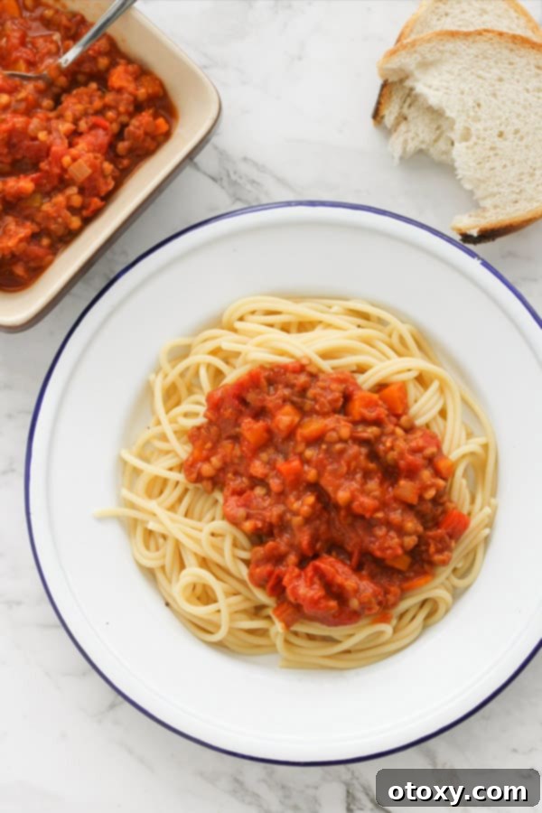 Rich and hearty lentil bolognese served over spaghetti on a white plate, garnished with fresh herbs.