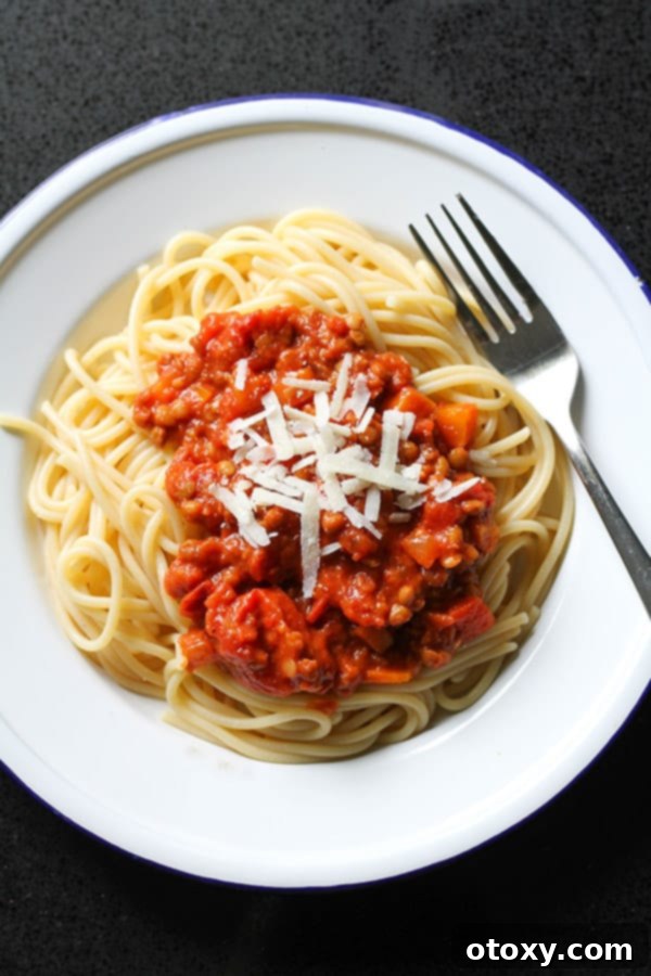 Close-up of lentil bolognese on top of spaghetti, topped with grated parmesan cheese and fresh basil.