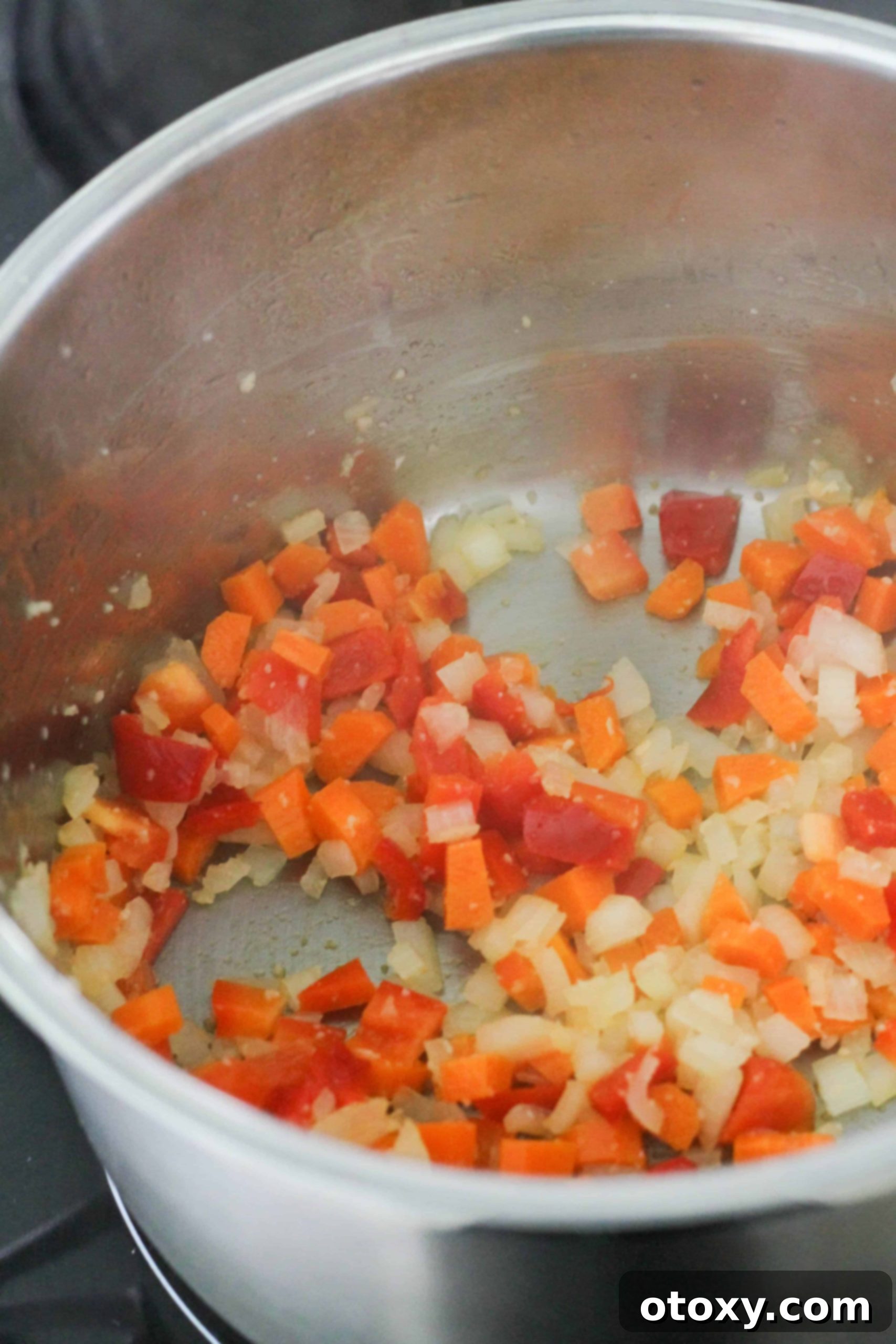 Colorful diced carrots and bell peppers being sautéed with onions and garlic in a large pot.