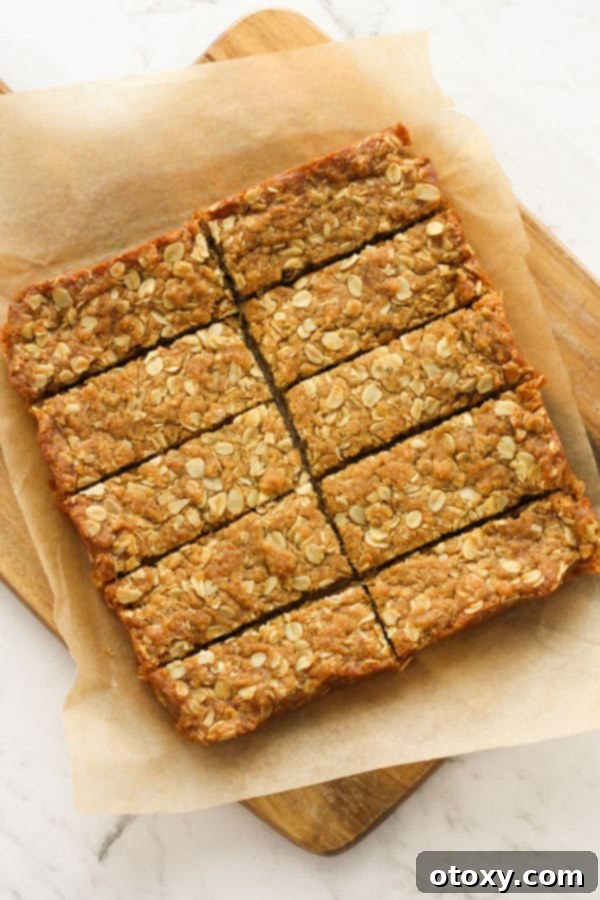 Anzac Golden Oat Bar 2 Freshly baked Anzac slices arranged neatly on a rustic wooden board, showcasing their golden-brown hue and irresistible texture.