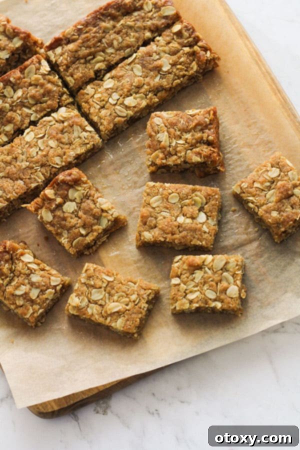 Anzac Golden Oat Bar 3 Close-up of golden-brown Anzac slice squares on a wooden board, highlighting their chewy texture and golden edges.