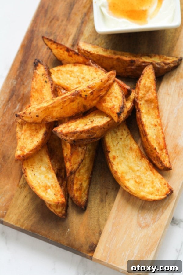 Air fryer potato wedges and dipping sauce on a wooden cutting board.