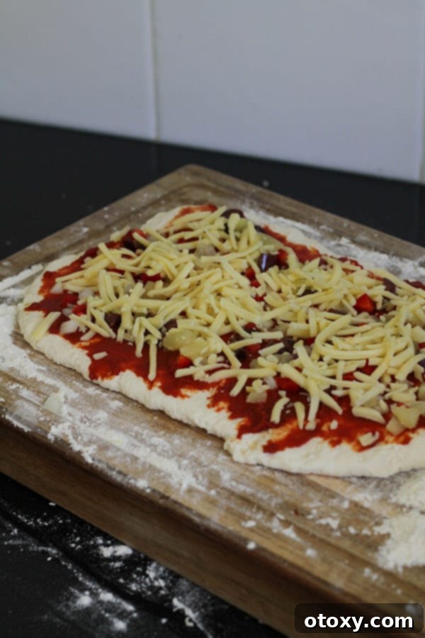 Dough covered with a vibrant array of vegetarian pizza toppings on a wooden board.