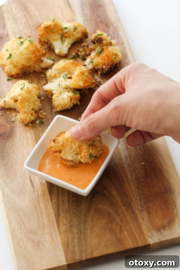Crispy Bang Bang Cauliflower Oven and Air Fryer 12 A hand gently dipping a crispy piece of Bang Bang Cauliflower into a small bowl of creamy, orange Bang Bang sauce.