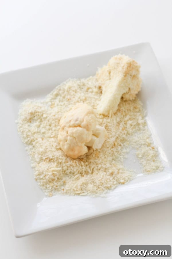 Crispy Bang Bang Cauliflower Oven and Air Fryer 5 Cauliflower pieces on a white plate, meticulously covered in panko breadcrumbs, ready for baking.