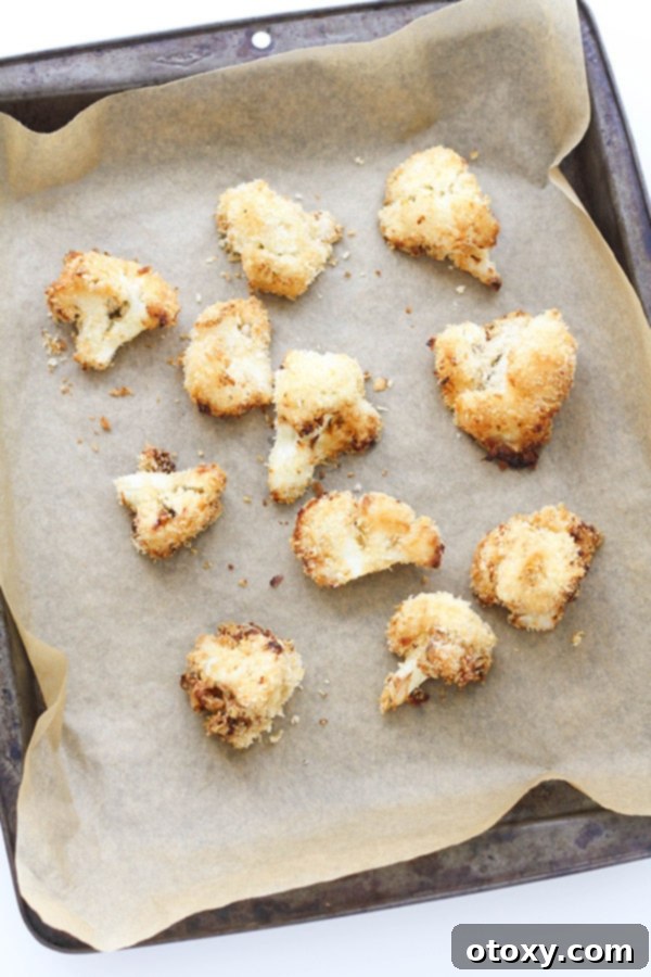 Crispy Bang Bang Cauliflower Oven and Air Fryer 7 Baked Bang Bang Cauliflower pieces, golden and crispy, fresh out of the oven on a baking tray.