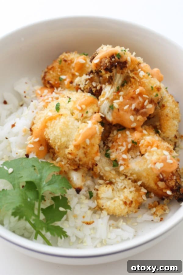 Crispy Bang Bang Cauliflower Oven and Air Fryer 8 A vibrant bowl of Bang Bang Cauliflower served with fluffy rice and fresh greens, drizzled with sauce.