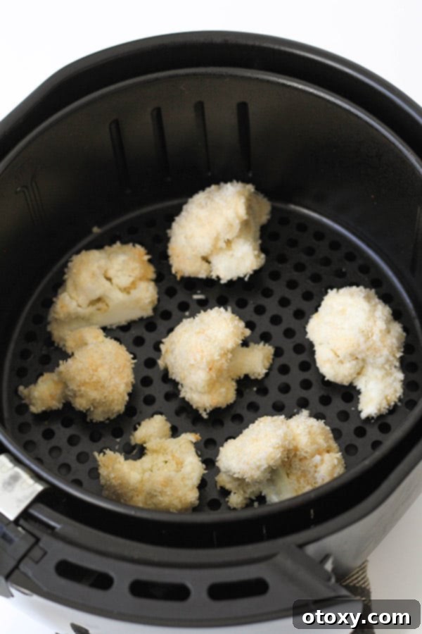 Crispy Bang Bang Cauliflower Oven and Air Fryer 9 Breaded cauliflower pieces meticulously arranged in an air fryer basket, ready for cooking.