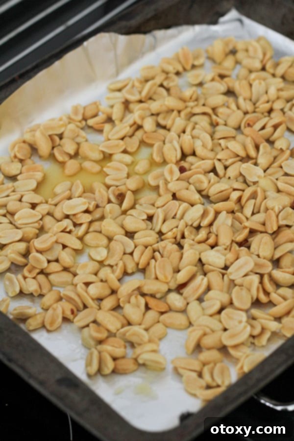 Easy Honey Roasted Peanuts in Your Oven or Air Fryer 6 Honey-coated peanuts spread in a single layer on a foil-lined baking tray, ready for oven roasting.