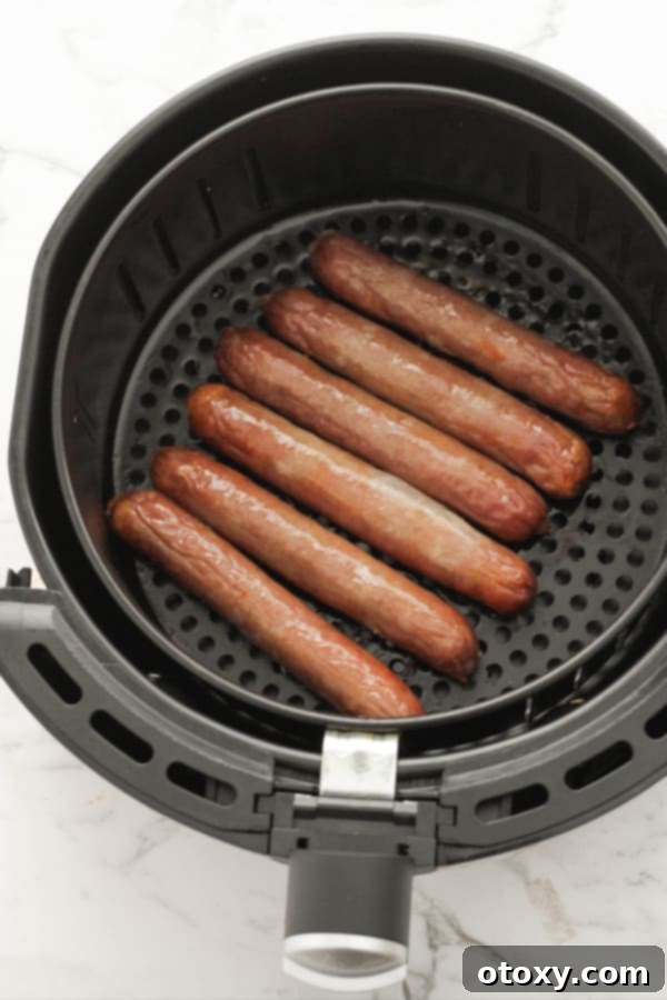 Golden-brown, perfectly cooked sausages in an air fryer basket, steam rising.