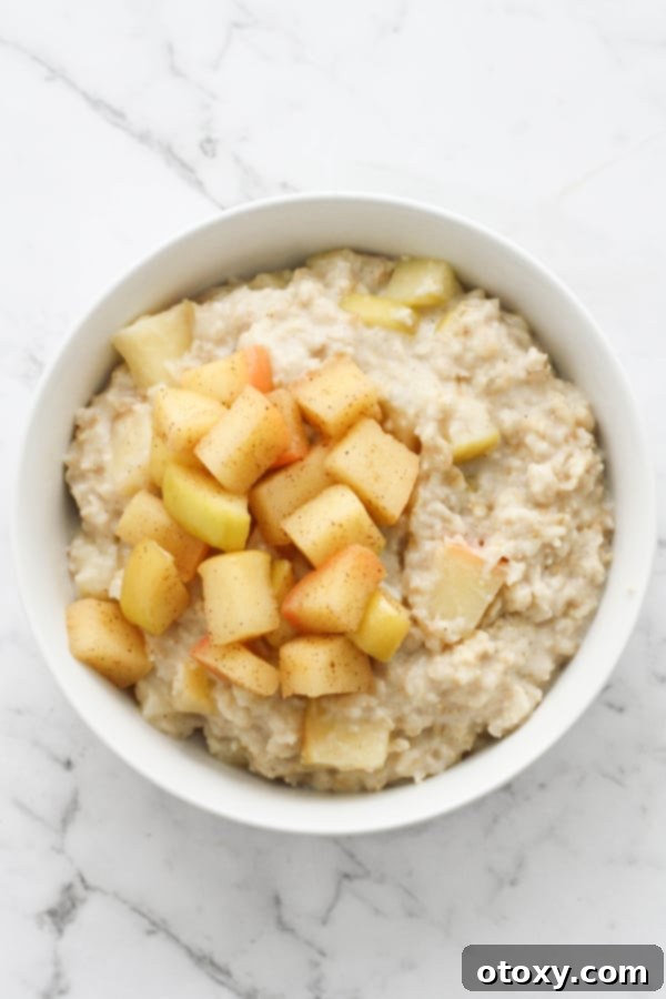 Harvest Apple Cinnamon Oats 2 A beautiful white bowl filled with creamy apple cinnamon oatmeal, generously topped with tender, stewed apple pieces and a sprinkle of cinnamon, ready to be enjoyed.