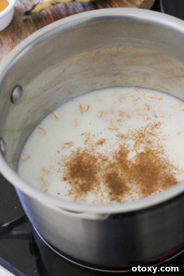 Golden Banana Breakfast Bowl 5 A saucepan on the stove filled with rolled oats, milk, and a sprinkle of cinnamon, beginning to simmer.