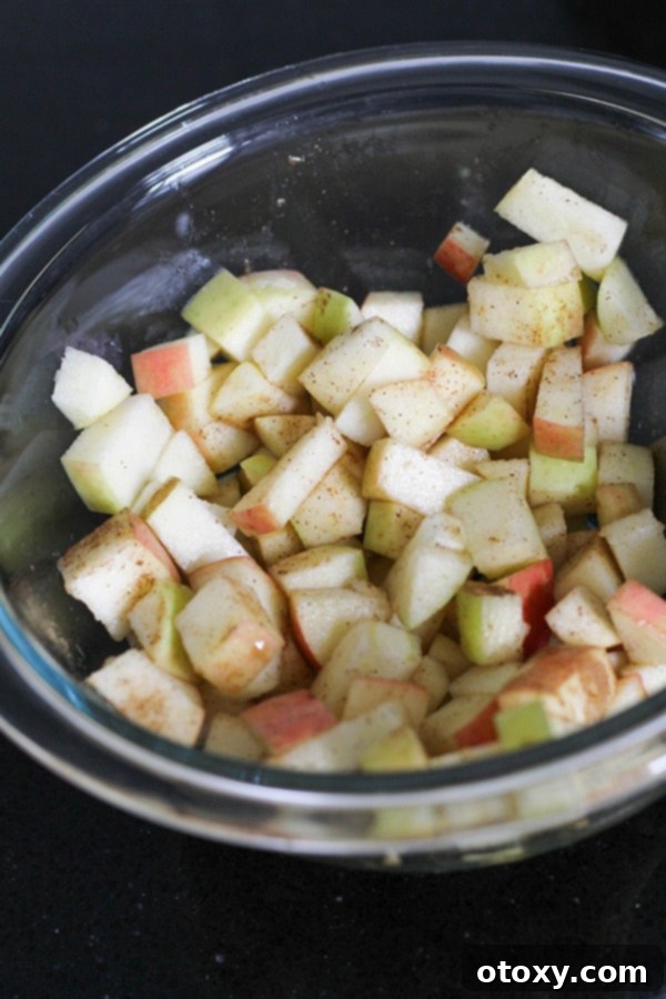 Diced apples mixed with spices and maple syrup in a clear glass bowl, ready for ramekins.