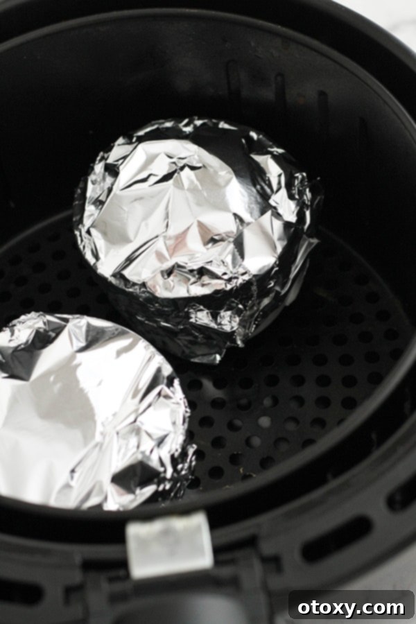 Two white ramekins, each covered with aluminum foil, placed inside an air fryer basket.