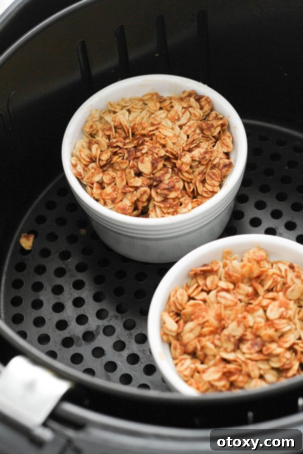 Two individual air fryer apple crisps, freshly cooked with golden brown topping, in an air fryer basket.