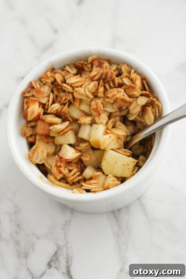 Air fryer apple crisp in a white ramekin, topped with a spoon, highlighting its warm, inviting appearance.