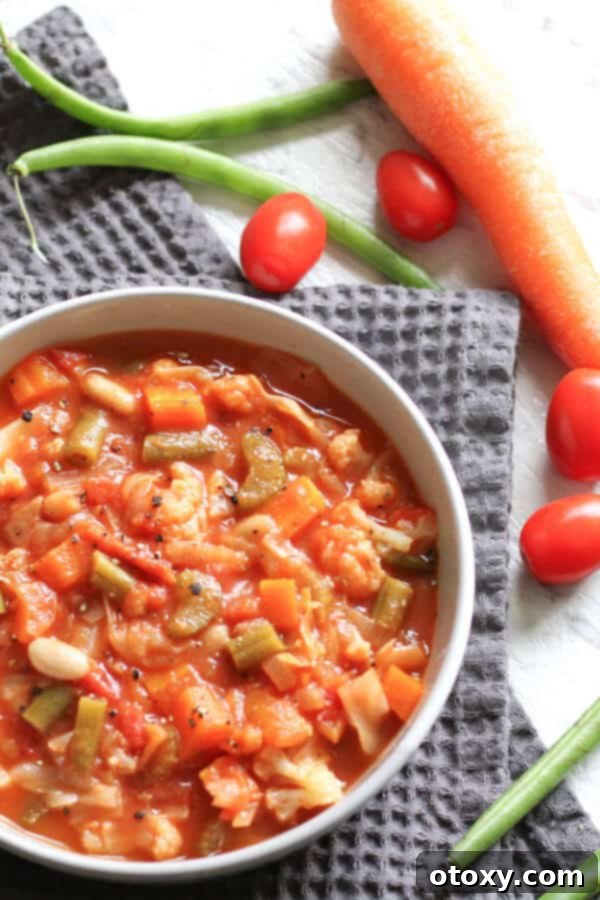cannellini bean soup in a white bowl surrounded by tomatoes, carrots and beans