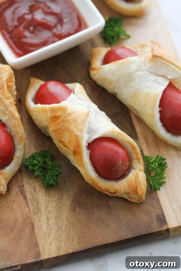 Crispy Air Fryer Sausage Bites 3 Perfectly golden and crispy pigs in a blanket on a wooden serving board, air fried to perfection.