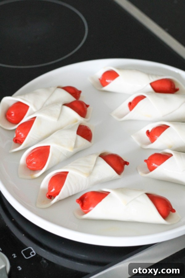 Crispy Air Fryer Sausage Bites 6 Several cocktail frankfurts, neatly wrapped in puff pastry and arranged on a plate, brushed with egg wash.