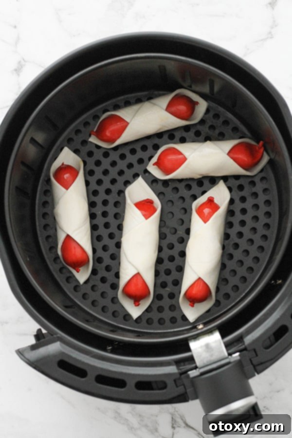 Crispy Air Fryer Sausage Bites 7 Air Fryer Pigs in a Blanket arranged in a single layer inside an air fryer basket, ready for cooking.