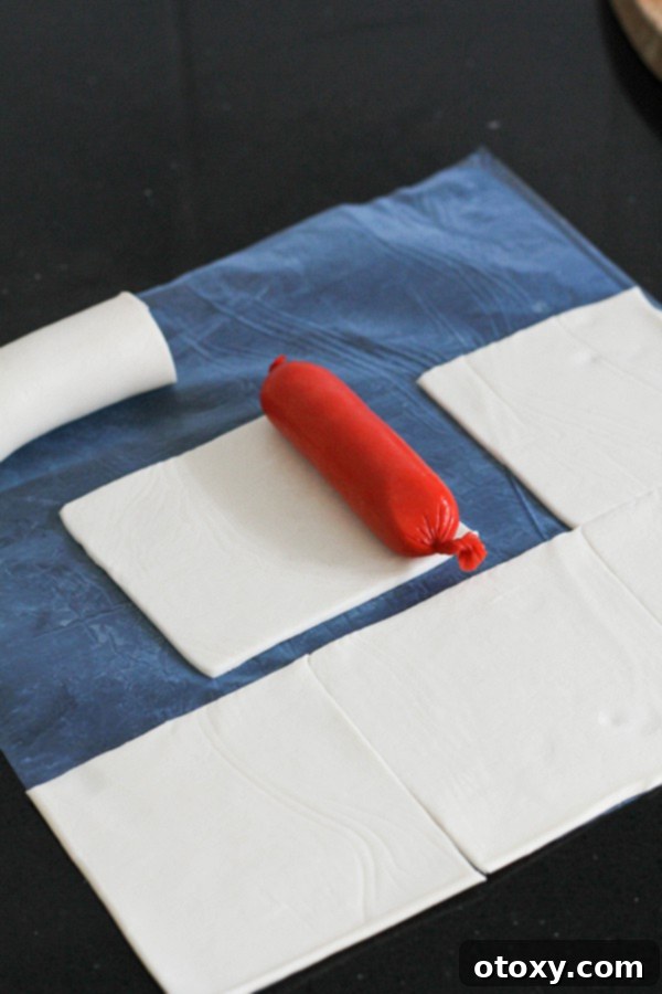 A mini hotdog placed on a square of puff pastry, ready for wrapping.