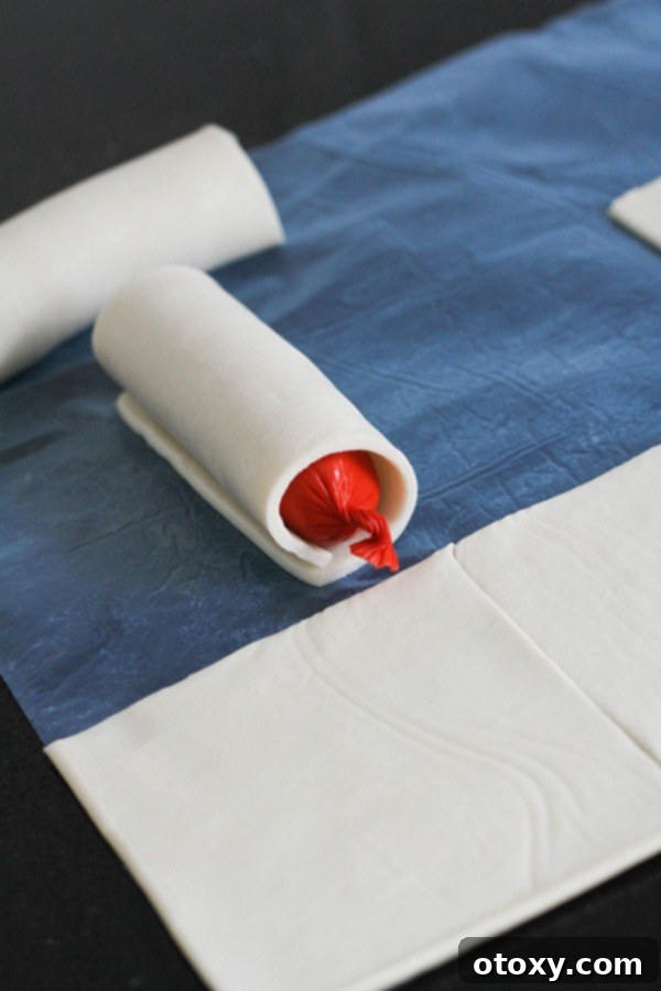 A mini hotdog perfectly wrapped in a puff pastry square, sealed and ready for baking.