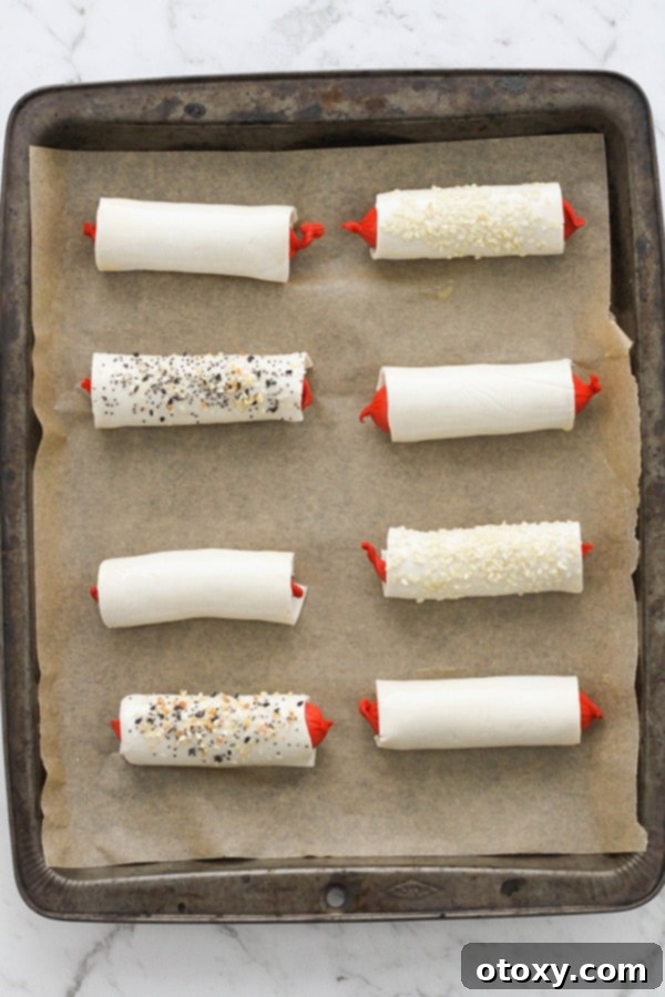 Several puffy dogs arranged on a baking tray, brushed with egg wash and sprinkled with toppings, ready for the oven.