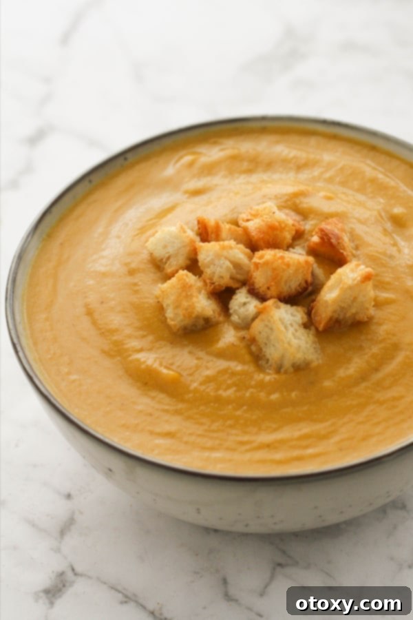 A close-up shot of creamy pumpkin and cauliflower soup in a bowl, generously topped with crispy golden croutons.