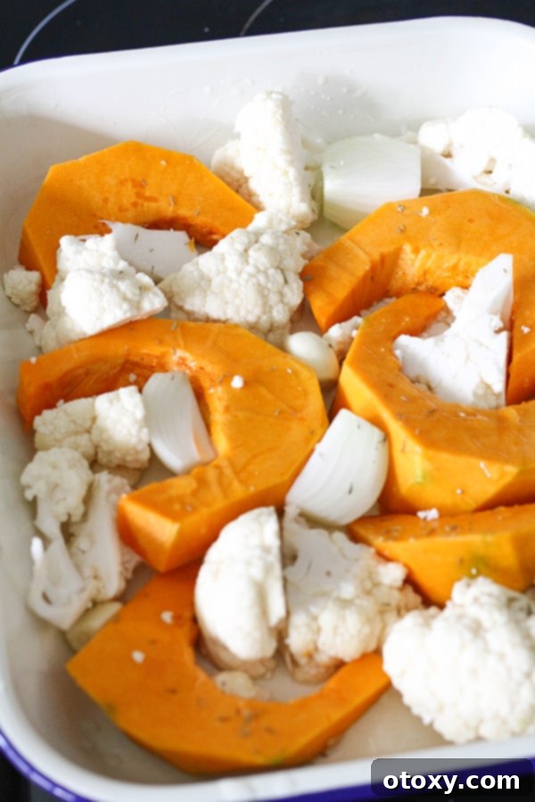 Chunks of pumpkin and cauliflower, along with onion and garlic, are spread out on a baking tray, ready for roasting to enhance their flavor.