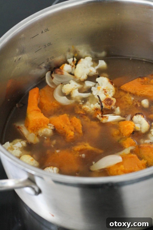 Roasted pumpkin and cauliflower are combined with vegetable stock in a large pot on the stove, ready to simmer and infuse flavors.