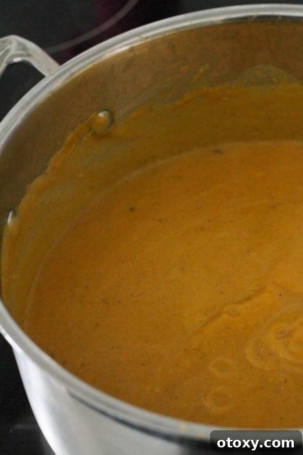 The finished, smooth, and creamy pumpkin and cauliflower soup sits ready in a large pot, steaming gently.