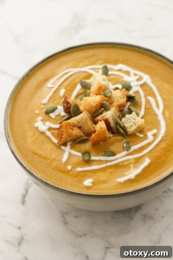 A bowl of pumpkin and cauliflower soup, elegantly garnished with crunchy croutons and a sprinkle of roasted pumpkin seeds, ready to be enjoyed.