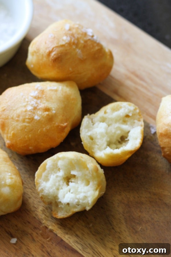 A freshly baked two-ingredient dough pretzel bite, perfectly split in half to reveal its soft, airy interior, resting delicately on a rustic wooden serving board.