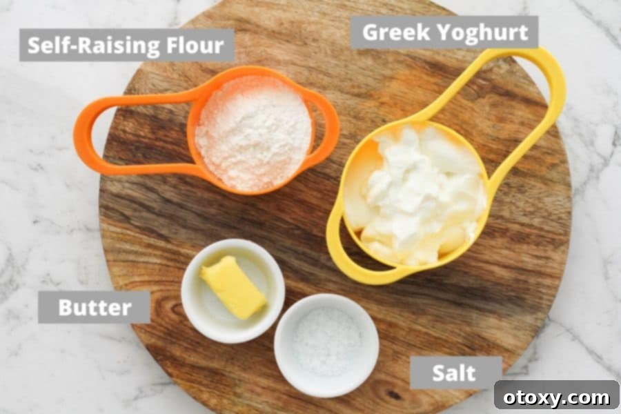 A flat lay photograph displaying the four simple ingredients required for pretzel bites: a bowl of Greek yogurt, a bag of self-raising flour, a stick of butter, and a container of pretzel salt.