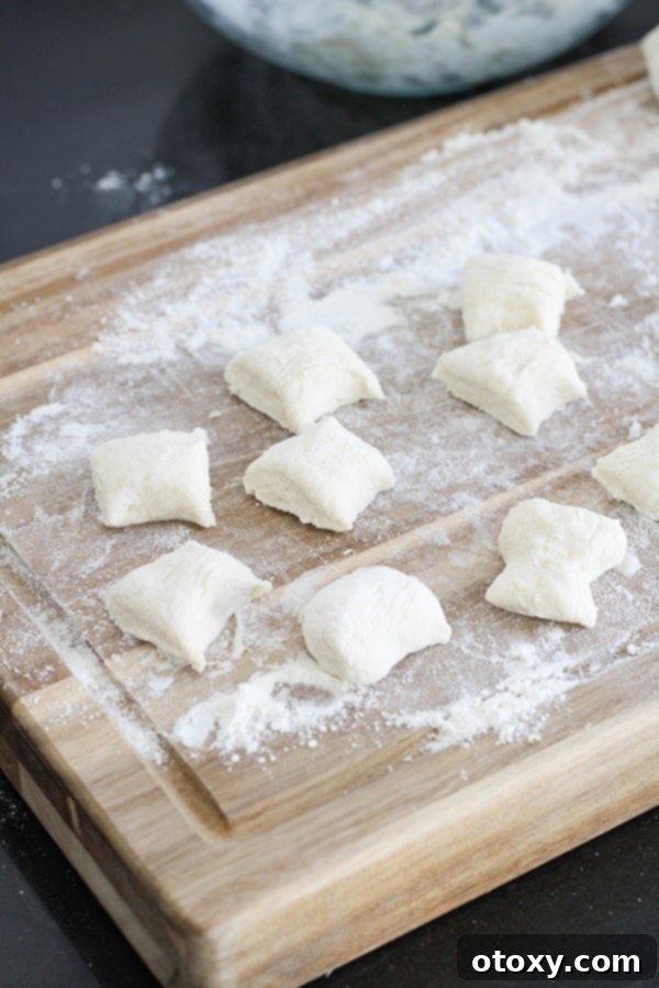 Dough rolled into ropes and cut into uniform, bite-sized pretzel pieces, neatly arranged on a wooden cutting board.