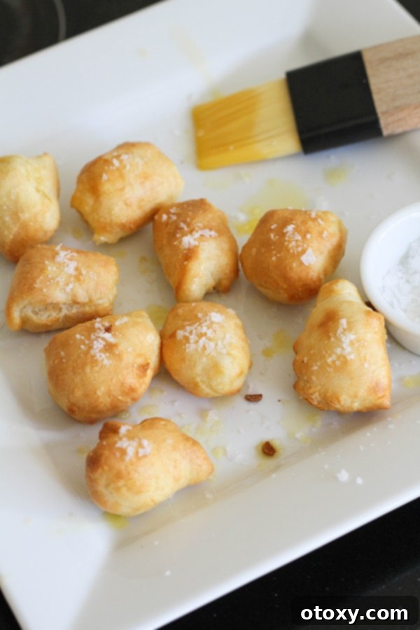 Warm pretzel bites beautifully arranged on a white plate, freshly brushed with melted butter and generously seasoned with coarse salt.