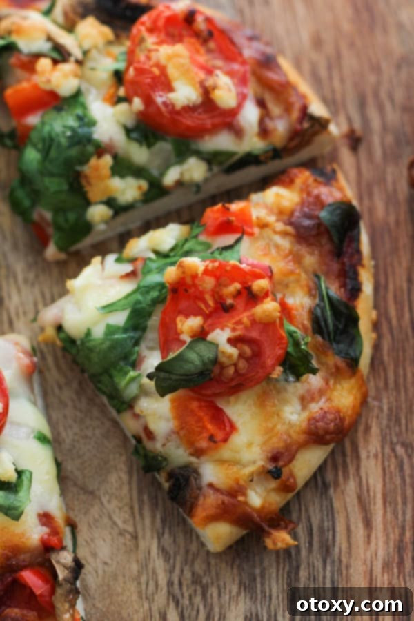 Mediterranean Greens and Feta Pizza 3 A perfectly baked slice of spinach and feta pizza, showing melted cheese and fresh toppings, on a wooden board.