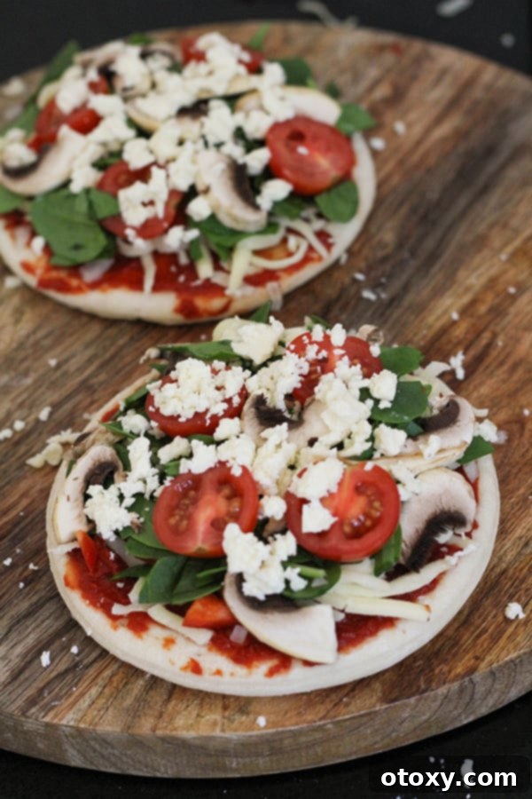 Mediterranean Greens and Feta Pizza 5 Two pizza bases topped with all ingredients, ready to be placed in the oven.