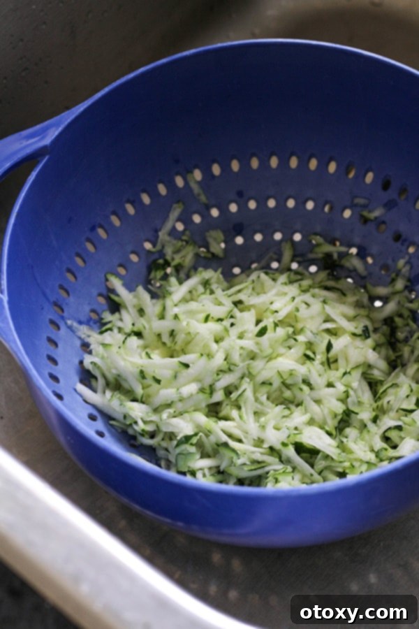 Close-up view of grated zucchini resting in a colander, showcasing the moisture being drained away.