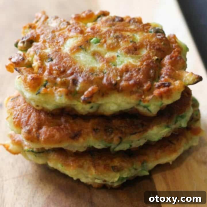 Pea & feta fritters beautifully stacked on a wooden serving board, showcasing their golden crispness.