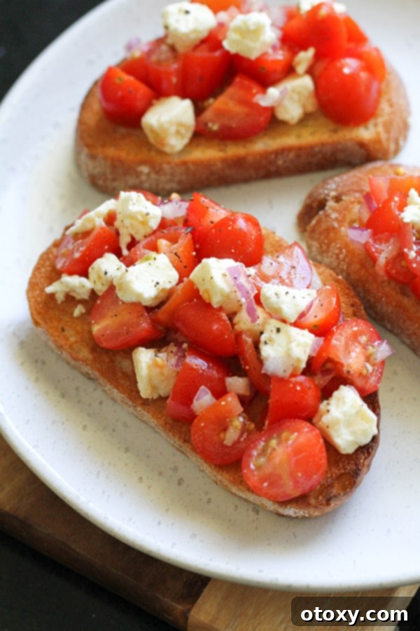 Fresh tomato and feta bruschetta drizzled with balsamic glaze, served on a pristine white plate.