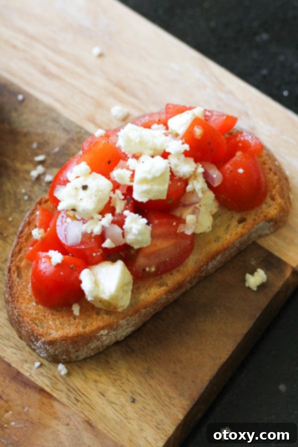 Multiple pieces of tomato and feta bruschetta neatly arranged on a rustic wooden serving board.