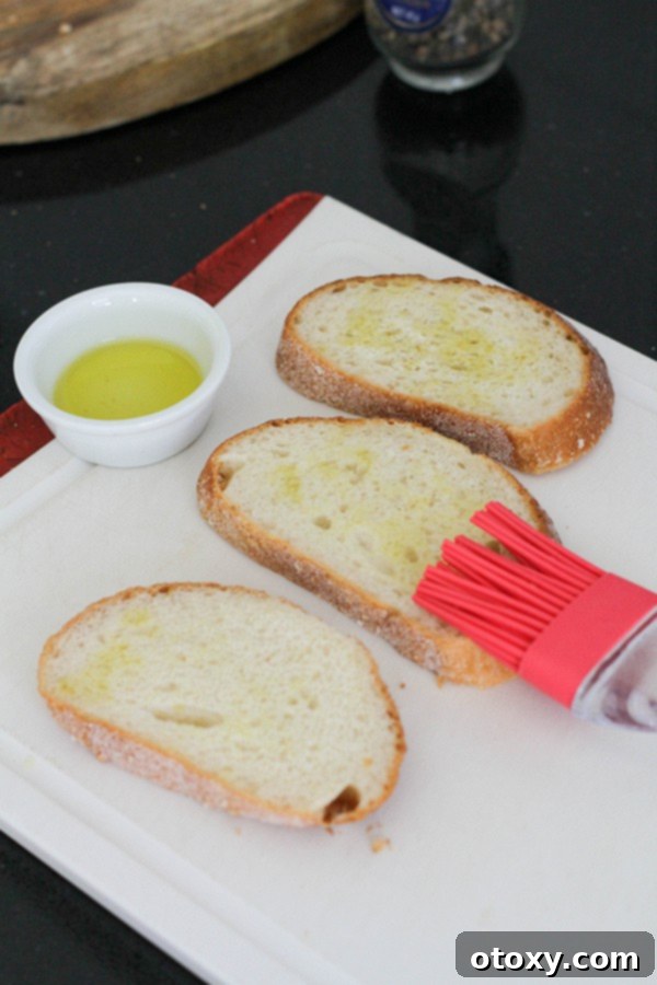 A pastry brush applying oil over slices of bread on a baking tray, preparing them for toasting.