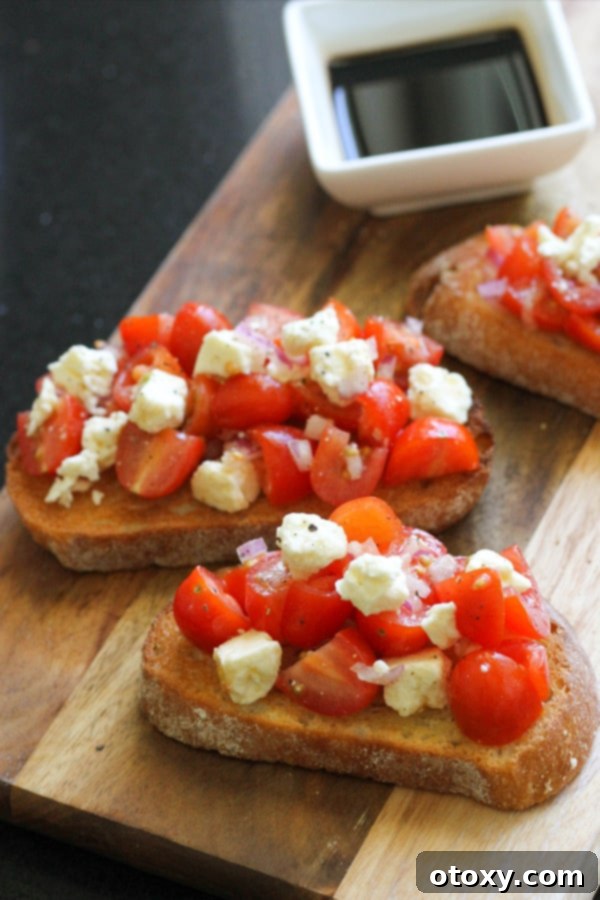 Beautifully plated tomato and feta bruschetta, drizzled with balsamic glaze, on a wooden serving board.