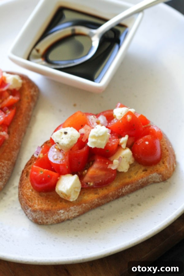 Close-up of tomato and feta bruschetta on a white plate, showing the vibrant colors and textures of the topping.